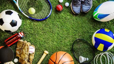 Image of assorted sports equipment around the perimeter of a green turf flooring. Items include a baseball bat, baseball glove/ball, a soccer ball, a tennis racket with a tennis ball, sneakers, etc.