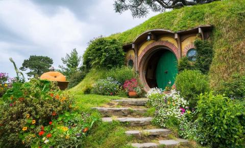 Image of Bilbo Baggins' House from the hobbit, stone pathway leading to a circular green door, lush with greenery around it.