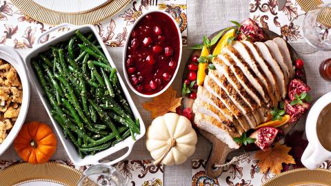 A festive table from an overhead view, decorated with pumpkins, fall napkins, and with asparagus, cranberry sauce, and sliced turkey on it.