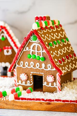 Image of a gingerbread house with a gumdrop walkway, twizzler fence, peppermint windows, and other red, green, and white candies decorating the roof in swirling patterns,