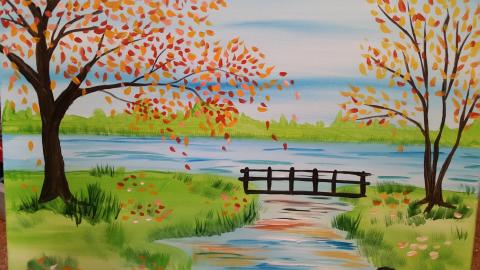 Image of the craft featuring a canvas painting showing fall trees and a small bridge over a river leading to a larger body of water. .