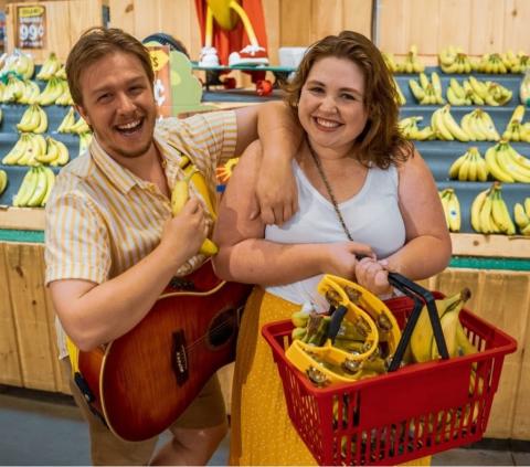 Image of the band members Ben and Anna in the Banana section of a grocery store. 