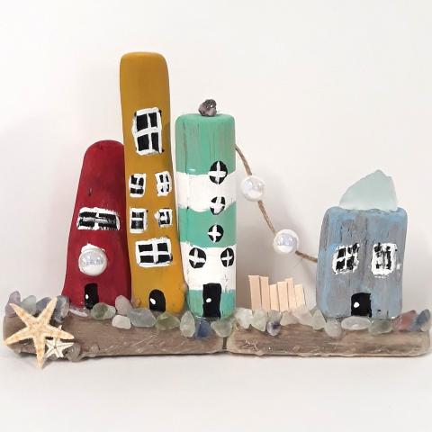 Image of the craft featuring painted pieces of driftwood made to look like little seaside homes with shells. 