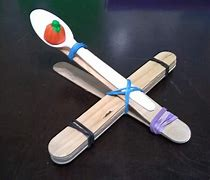 Image of the craft featuring a catapult designed out of a plastic spoon, tongue depressors and they are using small candy corn pumpkins as the "mini pumpkin"