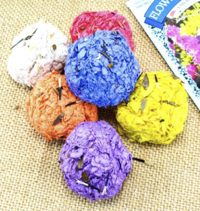 Colorful (orange, purple, blue, yellow, red, and white) seed bombs which look like balls of fabric on top of a brown cloth.