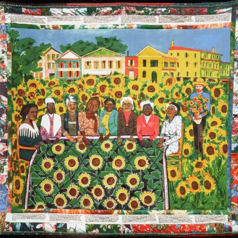 A Faith Ringgold quilt featuring women stitching a sunflower quilt together.