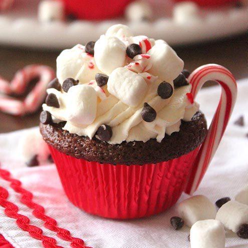 Image of a chocolate cupcake decorated to look like a hot chocolate with whipped cream and a candy cane handle. 