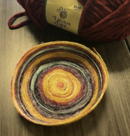 Yarn bowl made of yellow purple and blue threads on a wooden table.