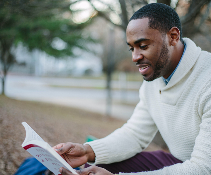 Man in sweater reading book outdoors